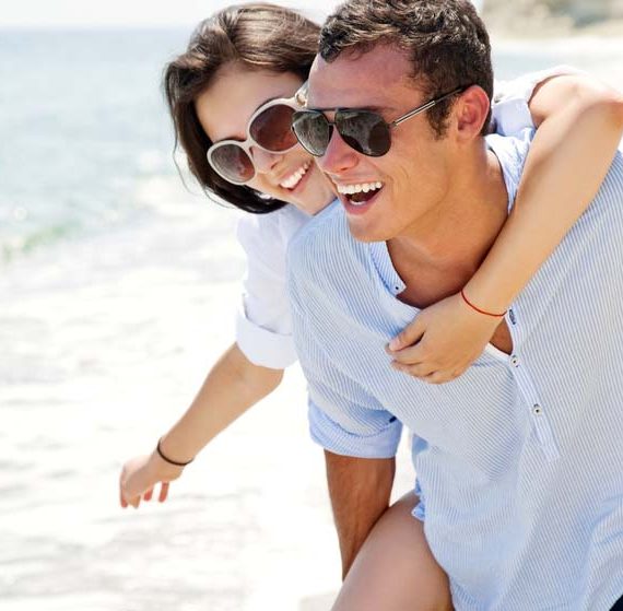 Smiling man giving a woman a piggyback ride on a beach