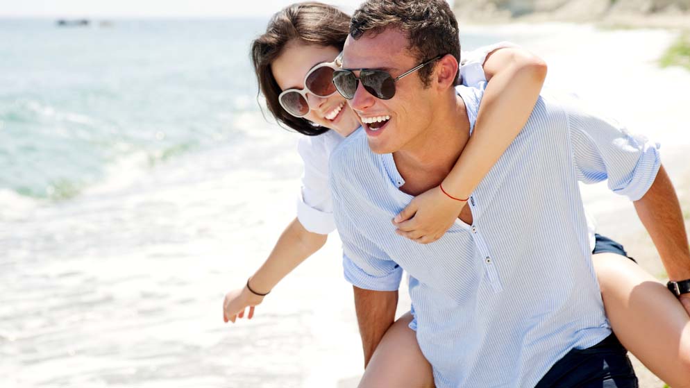 Smiling man giving a woman a piggyback ride on a beach