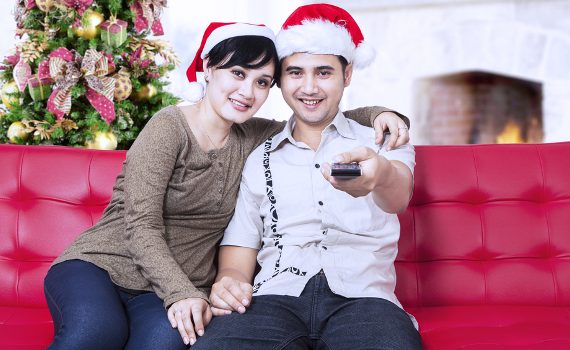 Happy christmas couple wearing santa's hats and holding a remote control