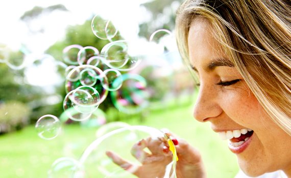 Happy woman portrait blowing soap bubbles at the park.