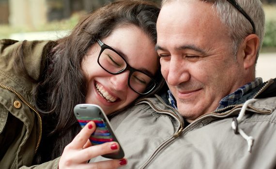 Father and daughter look at phone smiling and happy