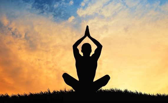 Person meditating against a sunset sky