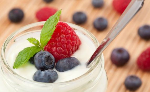 A jar of yogurt with berries and a spoon.