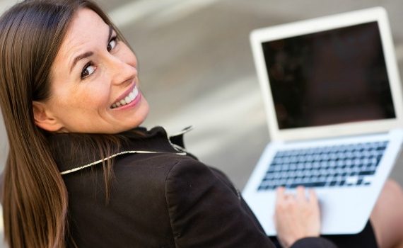 Smiling woman looking up from a laptop computer.