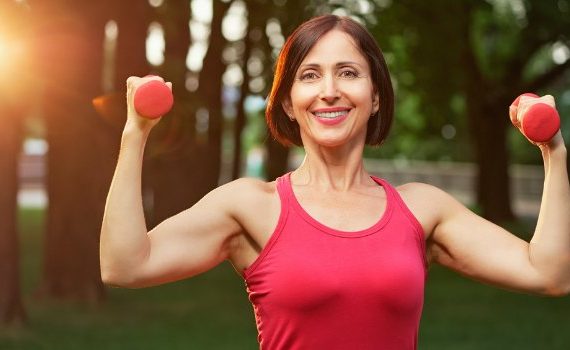 Happy 40-something woman lifting weights in the park.