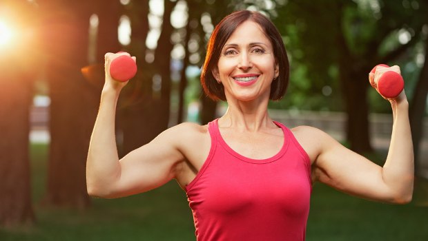 Happy 40-something woman lifting weights in the park.