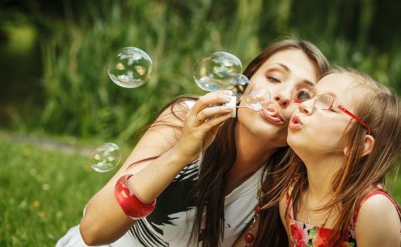 Happy mom and daughter blowing bubbles outside.