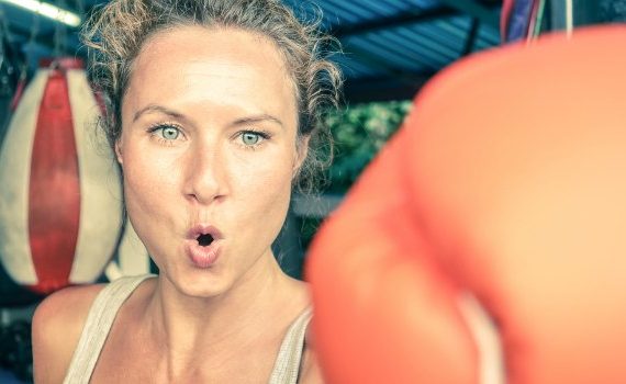 Woman boxing in a gym, gloved hand striking straight into the camera.