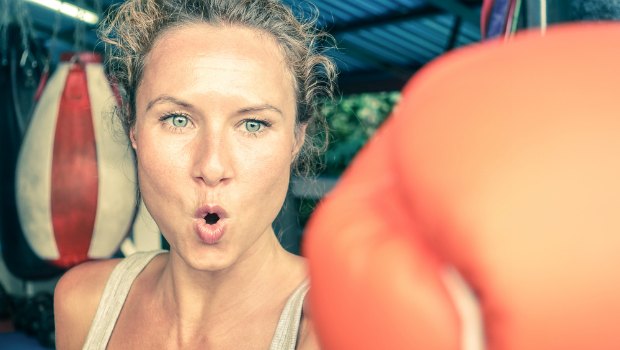 Woman boxing in a gym, gloved hand striking straight into the camera.