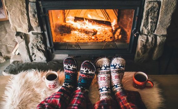 Two people warming their feet in front of a cozy fire.