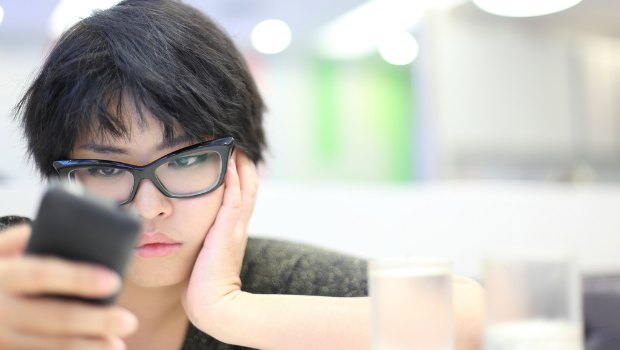 Young woman looking at her phone with irritated look on her face.