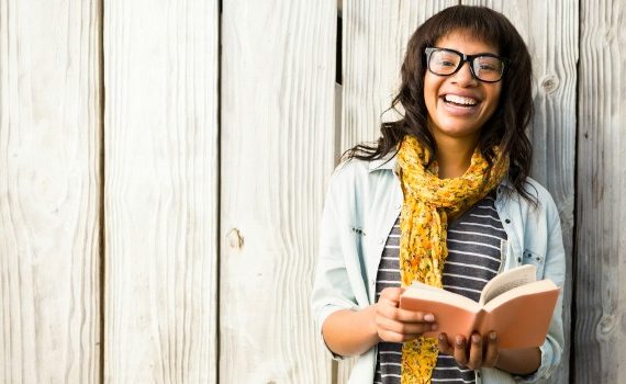 Young woman holding a book and smiling.