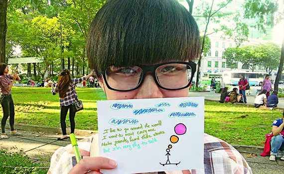 Boy with glasses holding up note and drawing.