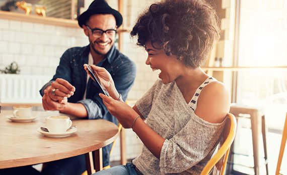 Two people looking at a phone and laughing in a cafe.