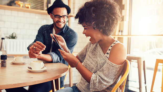 Two people looking at a phone and laughing in a cafe.