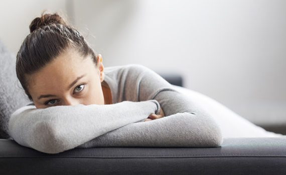 An anxious woman with her face hidden on a couch.