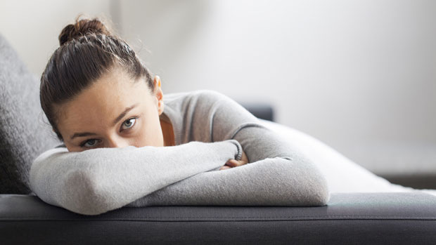 An anxious woman with her face hidden on a couch.