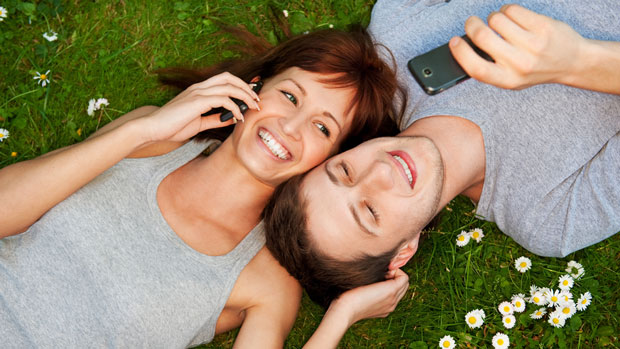 Couple lying on grass with phones.