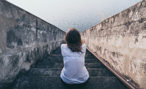 Woman sitting on steps next to the ocean.