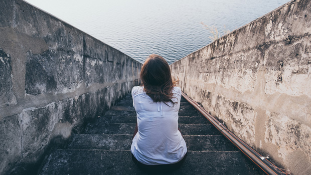 Woman sitting on steps next to the ocean.