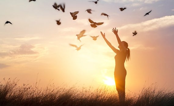 Woman holding her arms up and birds flying in night sky