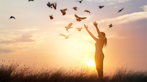 Woman holding her arms up and birds flying in night sky