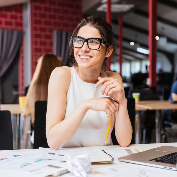 Portrait of smiling pretty young business woman in glasses sitting on workplace