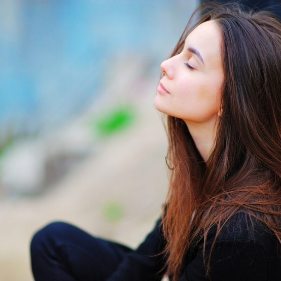 Portrait of a dreamy cute woman meditating outdoors with eyes closed, with the effect of blur, closeup.