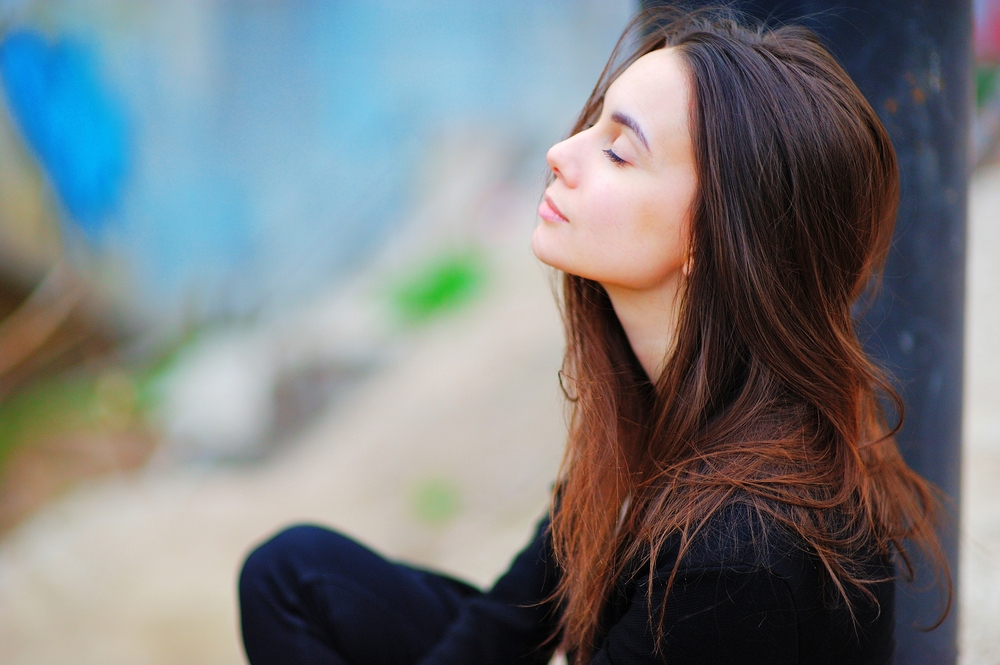 Portrait of a dreamy cute woman meditating outdoors with eyes closed, with the effect of blur, closeup.