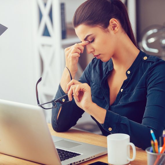 Feeling tired and stressed. Frustrated young woman keeping eyes closed and massaging nose while sitting at her working place in office