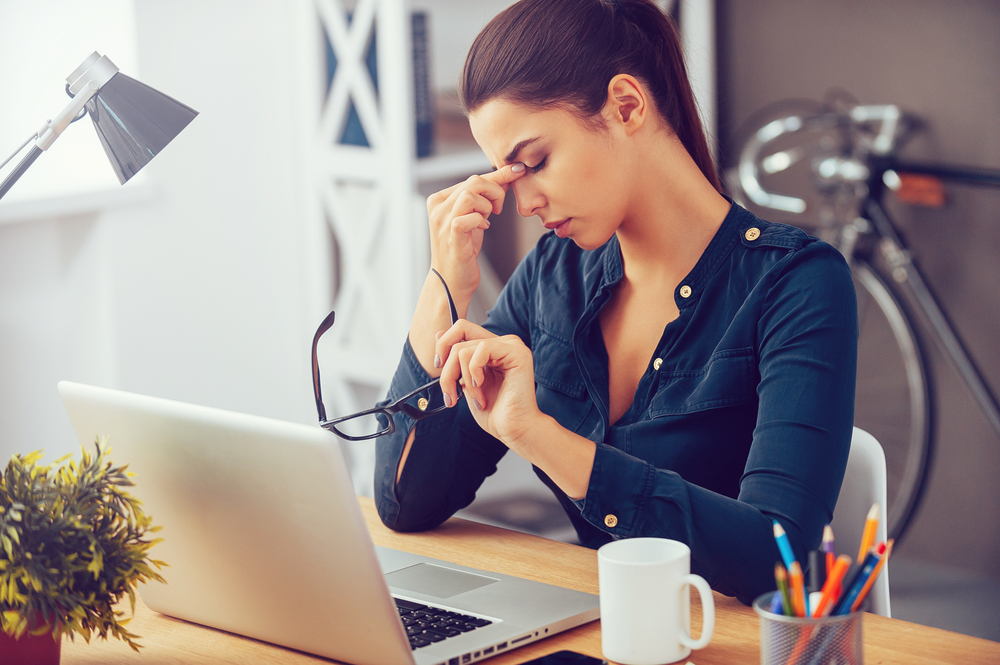 Feeling tired and stressed. Frustrated young woman keeping eyes closed and massaging nose while sitting at her working place in office