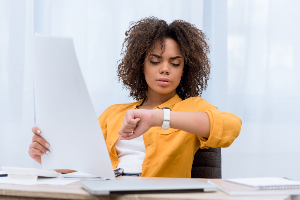 beautiful young woman working at office and looking at watch