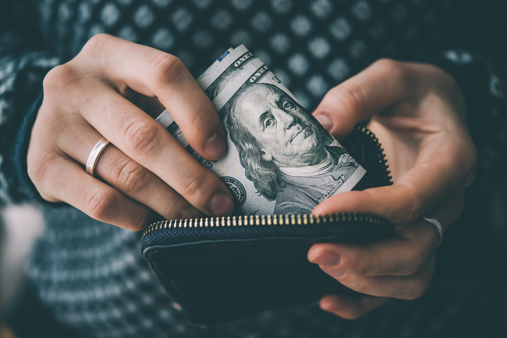 Hands holding us dollar bills and small money pouch.