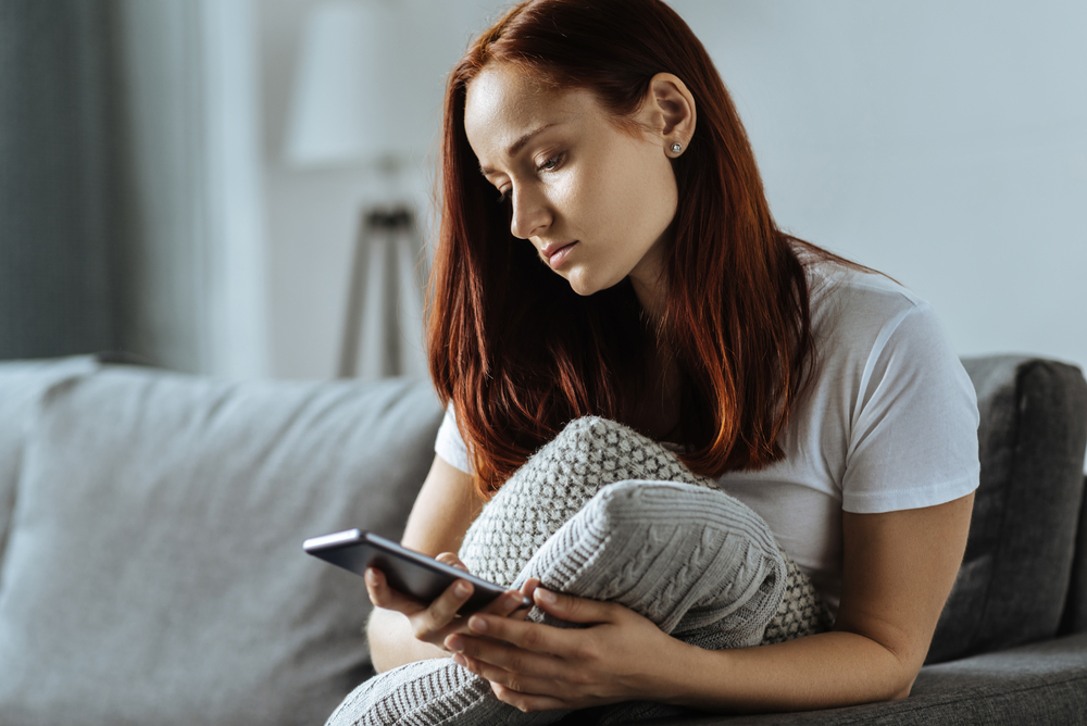 Sad young woman holding her smartphone