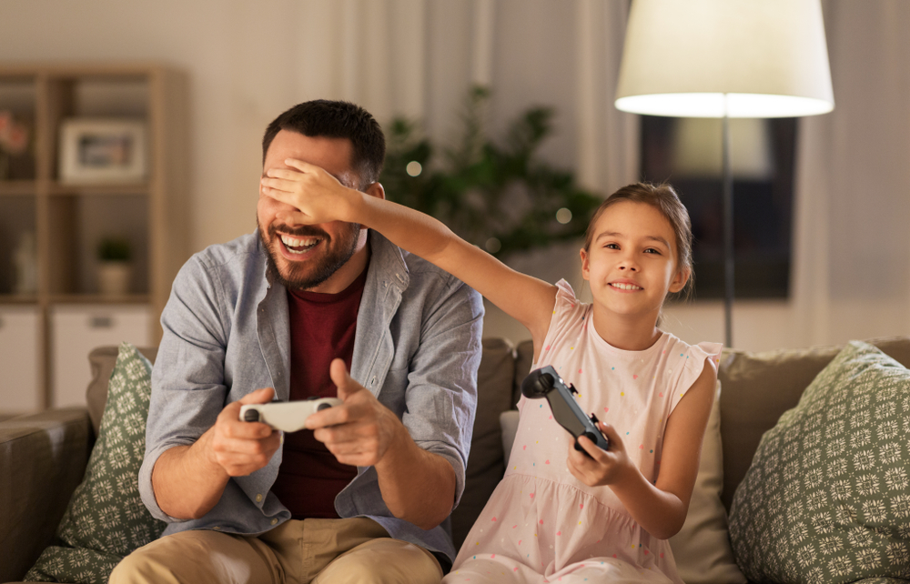 family, gaming and entertainment concept - happy father and little daughter with gamepads playing video game at home