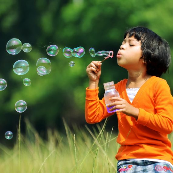 Children playing with soap bubbles on a green environment background