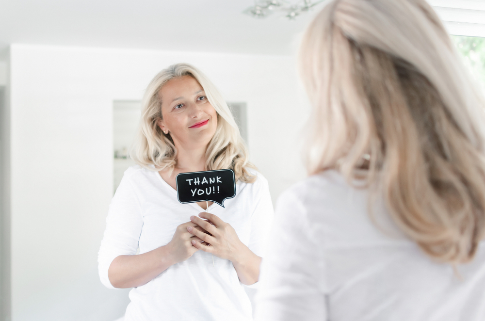 Beautiful adult woman smiling and holding photo prop in front of mirror at home