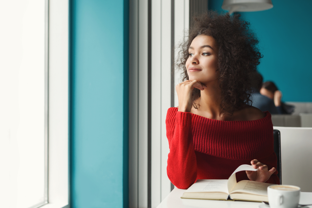 Young woman enjoying hot coffee and reading favorite book, looking at window.