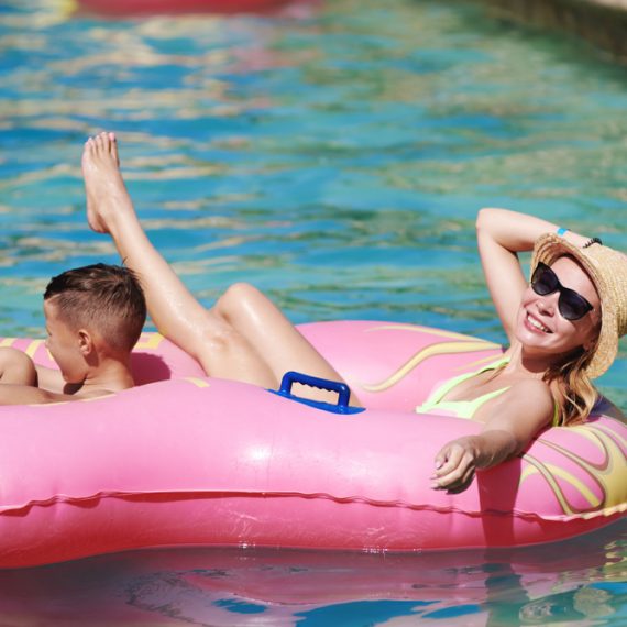 Mother and son enjoying their holidays in aqua park. They are swimming in a rubber ring along the lazy river, smiling and having fun.