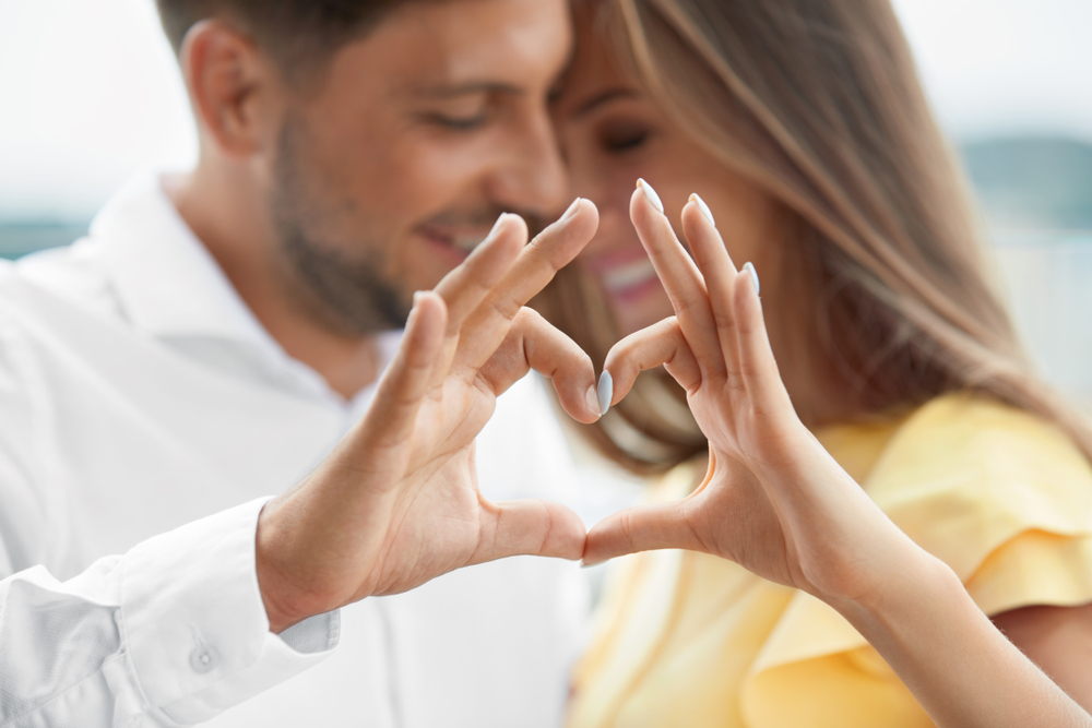 Happy Smiling Young People Hugging, Showing Heart Shape With Hands And Enjoying Each Other Outdoors.