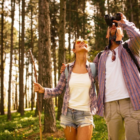 Young couple hiking trough forest and watching birds