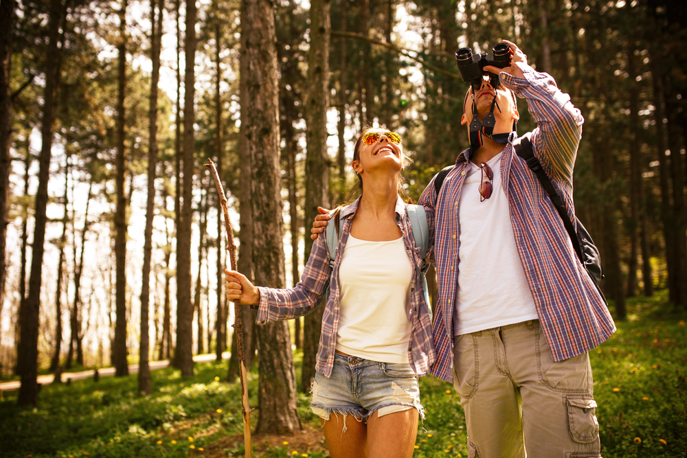 Young couple hiking trough forest and watching birds