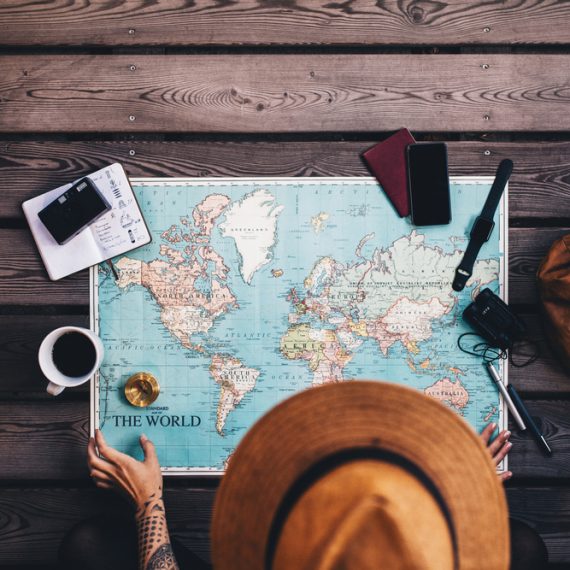 Young woman planning vacation using world map and compass along with other travel accessories. Tourist wearing brown hat looking at the world map.