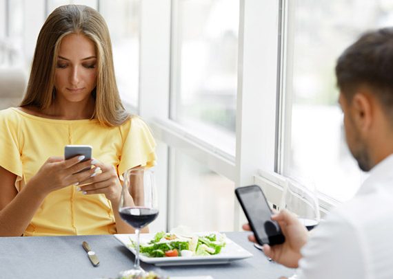 Man And Woman With Phones On Date. Young Couple Using Cell Phone On Dinner In Luxury Restaurant, Having Relationship Problems.