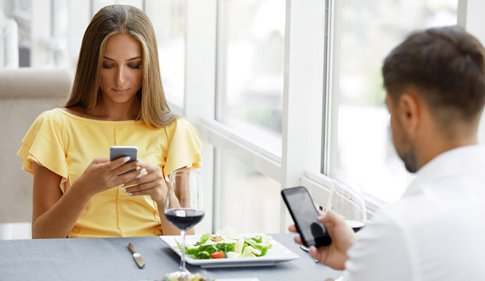 Man And Woman With Phones On Date. Young Couple Using Cell Phone On Dinner In Luxury Restaurant, Having Relationship Problems.