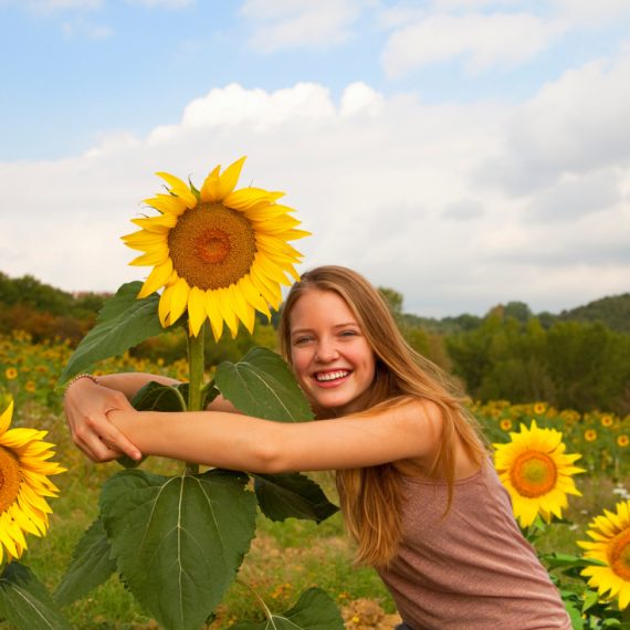 Teenage girl hugging sunflower in field