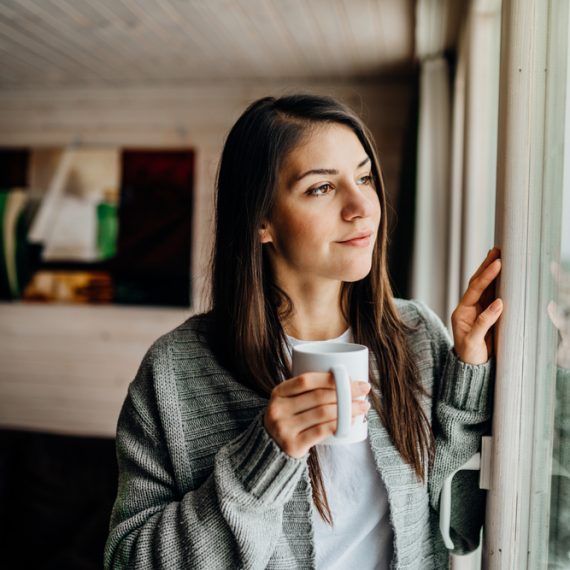 Young woman spending free time home.Self care,staying home. Enjoying view,gazing through to the window. Serene mornings.