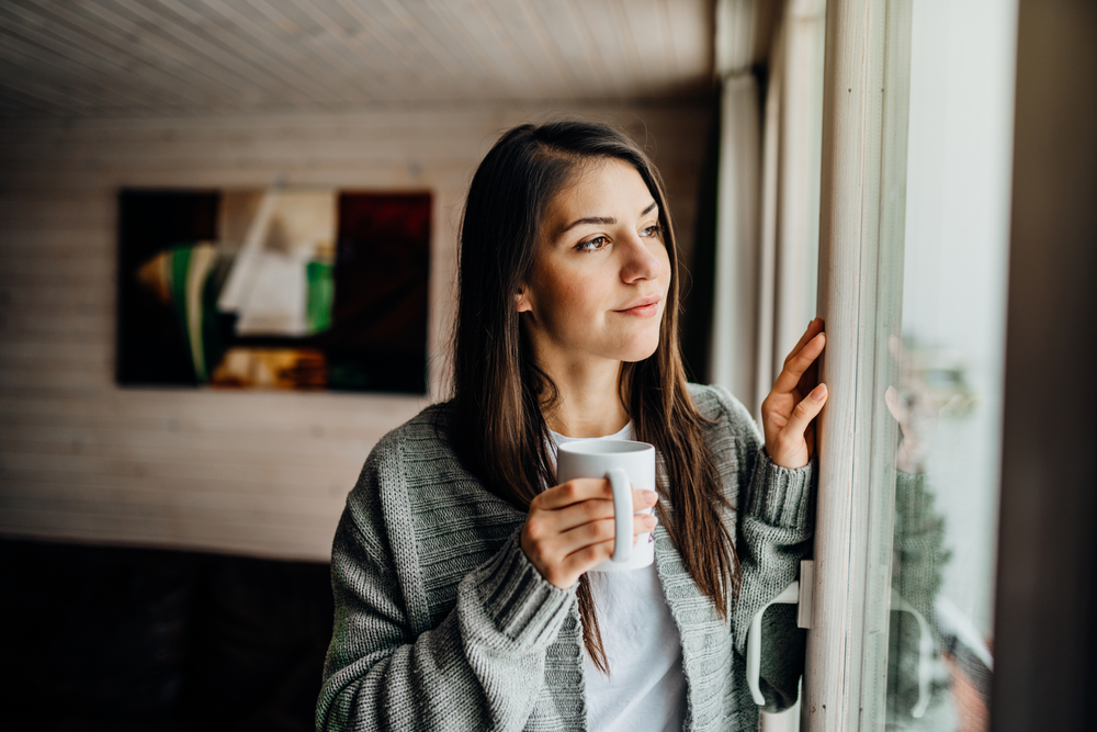 Young woman spending free time home.Self care,staying home. Enjoying view,gazing through to the window. Serene mornings.