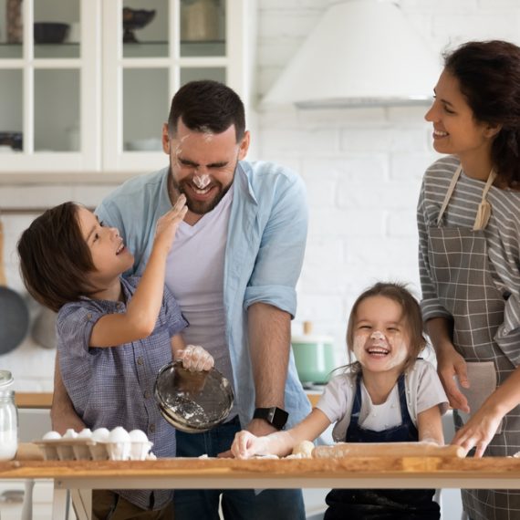 Overjoyed young family with little preschooler kids have fun cooking baking pastry or pie at home together, happy smiling parents enjoy weekend play with small children doing bakery cooking in kitchen