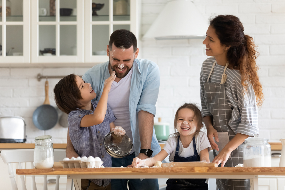 Overjoyed young family with little preschooler kids have fun cooking baking pastry or pie at home together, happy smiling parents enjoy weekend play with small children doing bakery cooking in kitchen